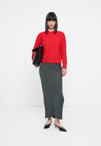 Red knitted sweater with rounded neckline, paired with a gray, fitted maxi skirt. Black handbag and pointed black heels complete the look.
