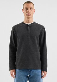 Czarna koszulka henley z długim rękawem, z trzema guzikami przy dekolcie, wykonana z miękkiego materiału, zestawiona ze jasnoniebieskimi dżinsami.