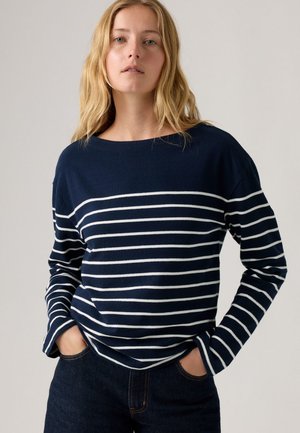 Top de manga larga azul marino con rayas horizontales blancas, escote redondo, corte relajado y textura suave. Combinado con pantalones de mezclilla oscuros.