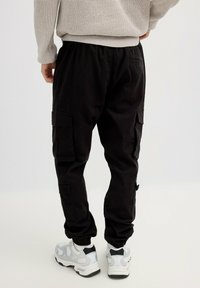 Pantalones cargo negros hechos de tela duradera, con puños elásticos y bolsillos laterales, combinados con zapatillas blancas y negras.