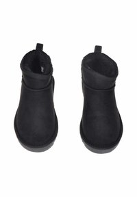 Stivaletti neri alla caviglia con esterno sintetico liscio, fodera morbida e un'etichetta a loop sul retro. Suole piatte e testurizzate per una buona aderenza.