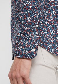 Camicia con bottoni, in tessuto leggero, con un motivo floreale blu navy che presenta fiori rossi, bianchi e blu; bottoni bianchi.