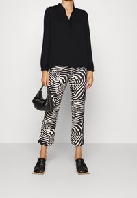 Blouse noire à manches longues avec un col henley, associée à un pantalon court imprimé zèbre noir et blanc et des sandales noires à lanières ouvertes.