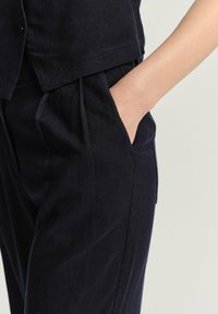 Námořnický lněný outfit s přiléhavým topem a volnými kalhotami s bočními kapsami, který se vyznačuje hladkou texturou a minimalisticým designem.