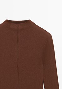 Brauner Pullover mit hohem Kragen. Gerippte Textur und eine zentrale Nahtdetail auf der Rückseite. Lange Ärmel, die bis zum Handgelenk reichen.