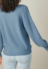 Pull côtelé bleu clair à manches longues avec une coupe décontractée. La texture semble douce, avec un large col et des poignets ajustés.