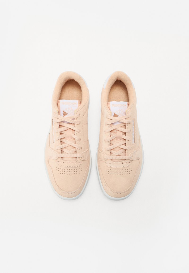 Zapatillas de ante melocotón claro con acentos blancos, punta redonda, diseño perforado, cordones planos y marca en la lengüeta y el costado.