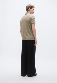 Polo bege com gola e mangas curtas, combinado com calças pretas de perna larga. Tecido liso com ajuste regular. Design simples.