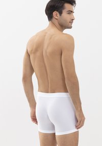 Weiße Baumwollboxershorts mit einem weichen Bündchen, figurbetontem Design und glatter Textur, von hinten an einem Modell betrachtet.