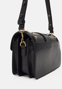 Svart läderaxelväska med gyllene spetsar upptill, avtagbar rem med knapppdetaljer och gyllene dragkedjehårdvara.