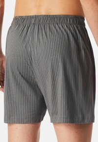 Costumi da bagno grigio a righe con vita elastica, caratterizzati da linee verticali in tonalità più scure e un tessuto liscio e leggero.