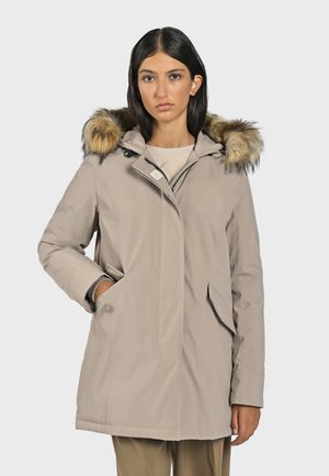 Giacca impermeabile beige con cappuccio foderato in pelliccia sintetica, zip e tasche laterali, dal taglio a lunghezza media e texture morbida.