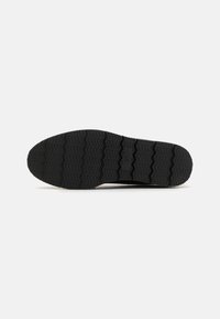 Semelle de chaussure de sport noire avec un motif en zigzag texturé pour l'adhérence, en matériau en caoutchouc, et un design plat et large pour la stabilité.