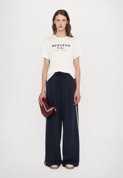 Weißes T-Shirt mit dem Aufdruck "WEEKEND MaxMara EST. 1983" in Schwarz, kombiniert mit navy-blauen weit geschnittenen Hosen und einer kleinen burgunderfarbenen Handtasche.