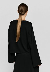 Schwarz, langärmliger, cropped Top aus einem weichen Stoff, mit lockerer Passform und weiten Ärmeln, kombiniert mit einem langen, fließenden Rock.