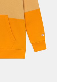 Felpa con cappuccio a blocchi di colore con sezione superiore beige, sezione inferiore arancione vivace, tasca frontale e polsini a costine. Il materiale è una morbida miscela di cotone.