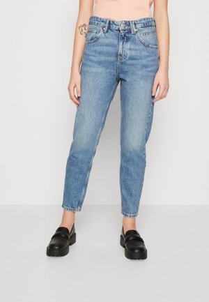 Jean en denim bleu clair avec une taille haute, des jambes droites et un design à cinq poches. Le tissu a une texture délavée. Associé à des mocassins noirs.