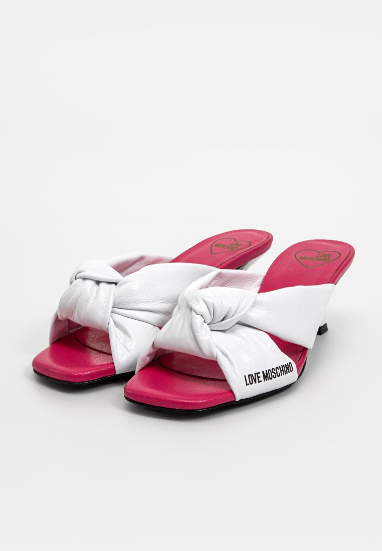 Weiße Leder-Sandalen mit einem geknoteten Riemen, ausgestattet mit einer rosafarbenen Innensohle und einem kleinen Absatz, mit dem Markennamen "LOVE MOSCHINO" an der Seite.