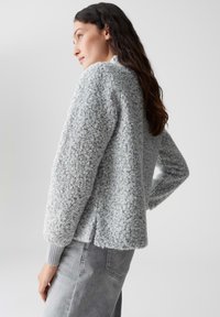 Hellgrauer, strukturierter Pullover mit einem weichen Boucle-Strickdesign, gerippten Bündchen und einer leicht verkürzten Länge. Die Rückansicht zeigt eine taillierte Form.