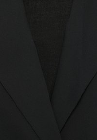 Sacou negru, confecționat dintr-un material neted, cu un luciu subtil, reveruri structurate și un strat inferior texturat negru. Marginile sunt ascuțite și curate.