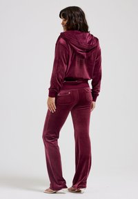 Velvet loungewear set in deep burgundy. Features a hooded sweatshirt and straight-leg pants with two back pockets and snap accents.