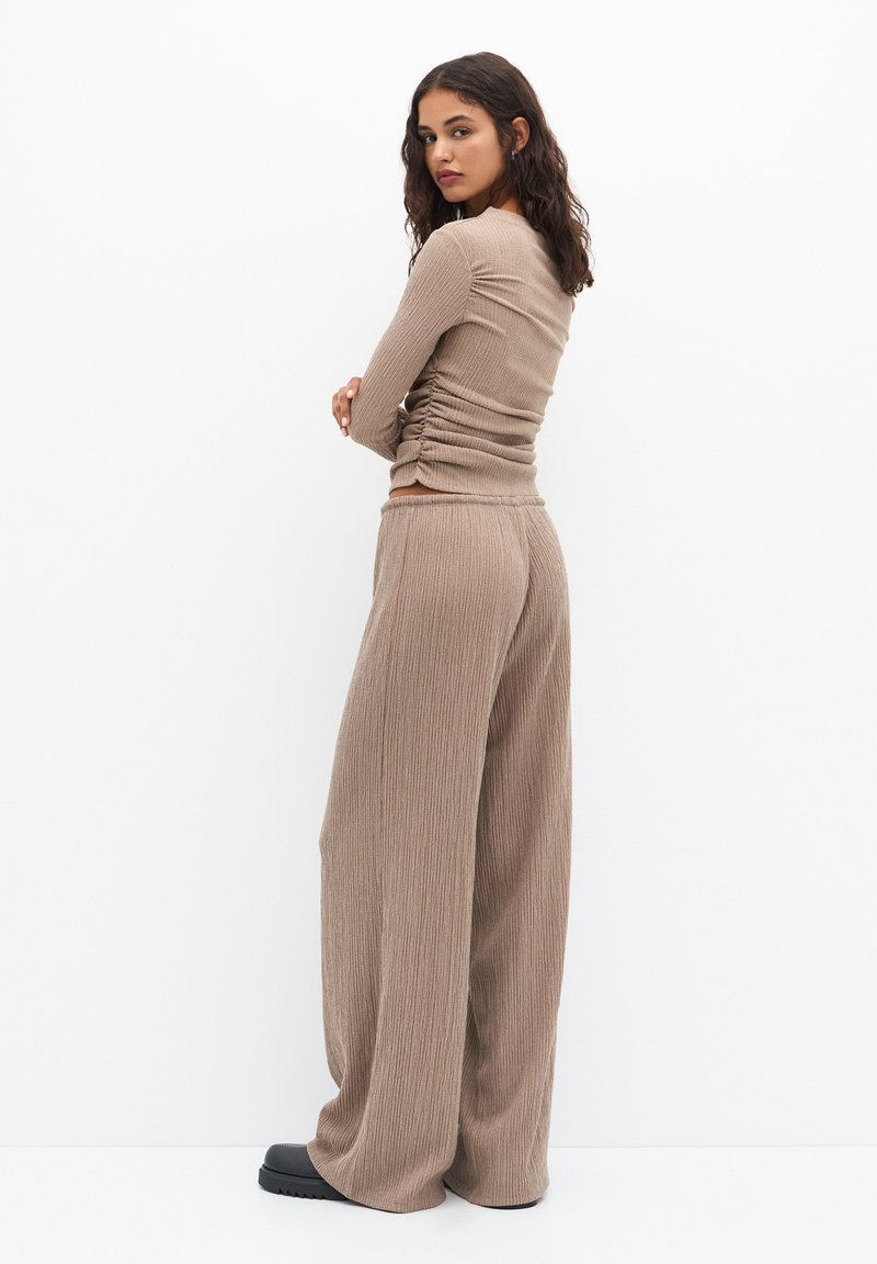 Top long à manches longues beige côtelé avec un détail froncé, associé à un pantalon large en tissu texturé identique, porté avec des chaussures à plateforme noires.