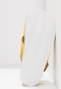 Sandale jaune avec semelle blanche texturée et boucle ajustable, présentée debout sur un fond blanc.