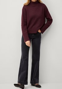 Pull à col roulé bordeaux avec poignets et ourlet côtelés, associé à un jean évasé noir et des chaussures plates noires. Texture lisse, coupe décontractée.