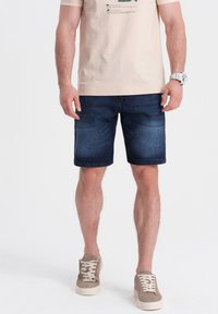 Shorts en denim bleu foncé à coupe droite, avec une l�égère décoloration. Assortis à un t-shirt en coton beige et des baskets lacées gris clair.
