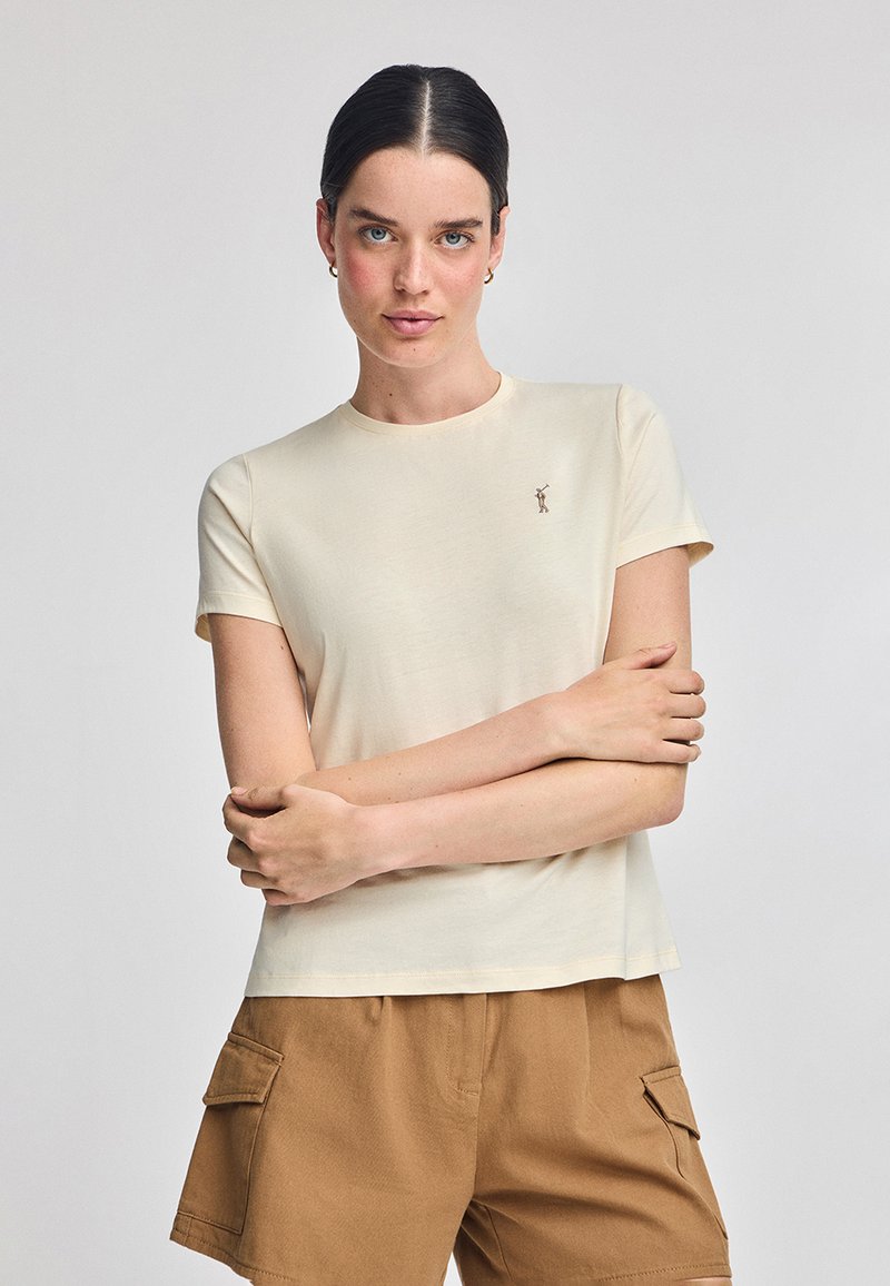 T-shirt in cotone beige chiaro con maniche corte, scollatura rotonda e un piccolo design ricamato sul petto. Tessuto liscio.