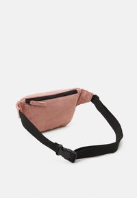 Marsupio in tessuto a coste rosa con zip nera e tracolla regolabile. Il design presenta una forma compatta e arrotondata per un facile trasporto.