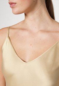 Camisole in satin di un morbido colore oro con scollatura a V e spalline sottili, che mette in mostra una texture liscia e una lucentezza sottile.