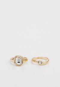 Zwei goldene Ringe: Der eine hat einen großen, klaren rechteckigen Stein; der andere hat einen kleineren quadratischen Stein. Beide haben eine glatte, glänzende Oberfläche.