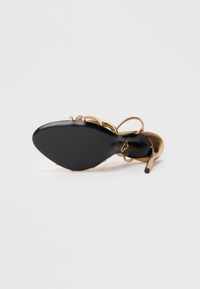 Hoge hak sandalen met een zwarte zool, gouden metalen bovenwerk en spiraal ontwerp voor de bandjes. Slanke, spitse neus en slanke hak benadrukken de silhouet.
