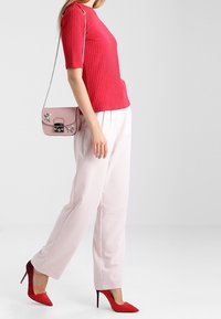 Top corto a maniche corte a coste rosse abbinato a pantaloni a gamba larga rosa chiaro. La modella porta una borsa rosa con dettagli floreali e indossa décolleté rosse con tacco a spillo.