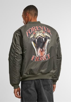 Olivengrønn bomberjakke med et stort slangegrafikk medåpen munn og røde detaljer, teksten "FOREVER FIERCE" over, ribbestrikkede mansjetter og kant.