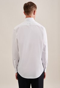 Witte blouse met lange mouwen, een gladde textuur, een afgeronde zoom en knoopsluitingen bij de manchetten. De achterkant toont een klassieke kraag en details van het shirtontwerp.