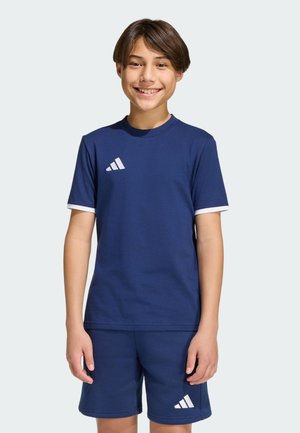 Ragazzo sorridente che indossa un completo sportivo Adidas blu navy, composto da una maglietta a maniche corte e pantaloncini abbinati con dettagli del logo bianchi.