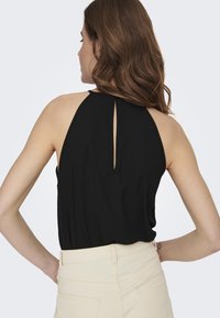 Top negro sin mangas con detalle de abertura en la espalda, hecho de una tela suave, con un corte holgado y textura suave. Combinado con pantalones de color claro.