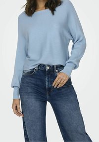 Light blue ribbed sweater with a wide neckline, paired with high-waisted dark blue jeans. Soft texture and relaxed fit.