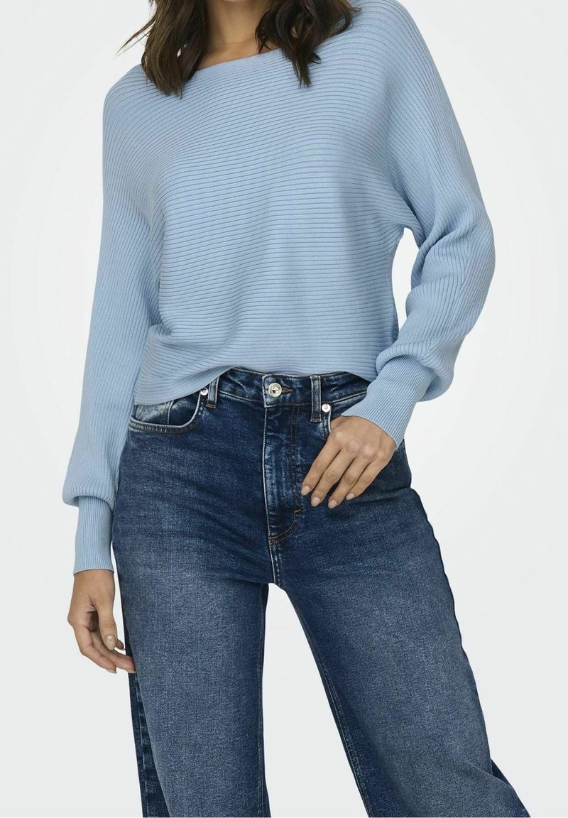 Light blue ribbed sweater with a wide neckline, paired with high-waisted dark blue jeans. Soft texture and relaxed fit.