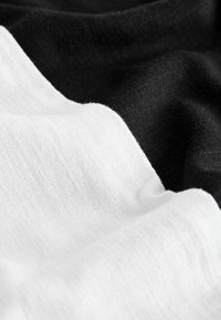 Black and white fabric draped together, featuring a smooth texture. The black side has a fine, slightly crisp weave, while the white side is softer.