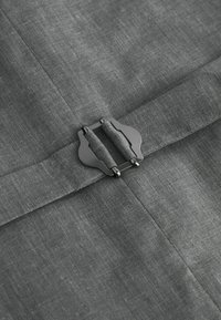 Tela gris con una textura sutil que presenta un broche central con acabado en metal cepillado, añadiendo un contraste frente al material.