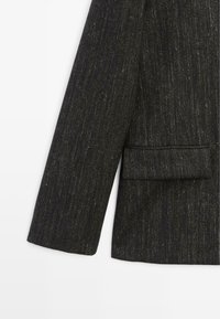 Donkergrijze blazer van een gestructureerde stof, met een enkele borstzak en een getailleerde snit met licht gestructureerde schouders.