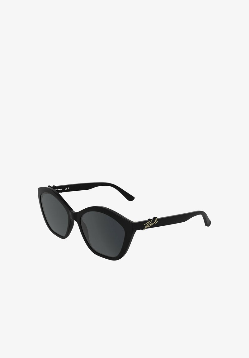Zwarte cat-eye zonnebril met donkere glazen en een gouden "Karl" handtekening op de pootjes, afgebeeld tegen een witte achtergrond.