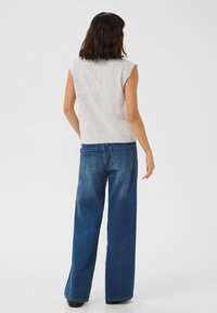 Haut sans manches gris clair avec un tricot texturé, associé à un jean en denim bleu à jambes larges, présentant des poches arrière et une coupe décontractée.