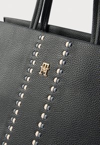 Fekete bőrtáska, amely texturált felülettel, váltakozó bézs és kék gyöngysorokkal és arany logó díszítéssel rendelkezik.