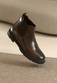 Brown leather ankle boot with elastic side panels, rounded toe, black rubber sole, and pull tab at the rear for easy wear.