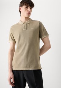 Khaki polo tričko s klasickým golierom, dvoma gombíkmi a krátkymi rukávmi. Obsahuje jemné logo na hrudi a mäkkú, textúrovanú tkaninu.