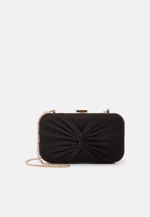 Zwarte rechthoekige clutch met stoffen knoopdetail, gouden frame en gouden kettingriem tegen een witte achtergrond.